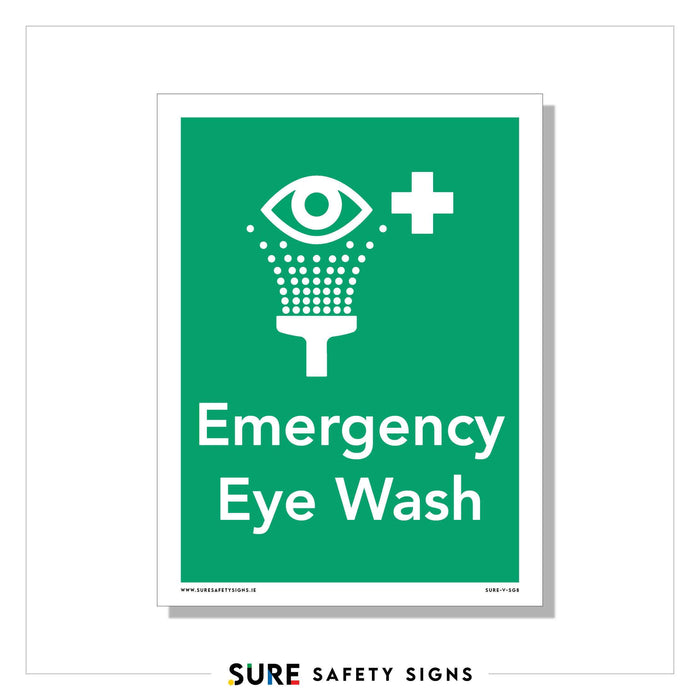 Green safety sign with a white icon of an eye above a showerhead, indicating an eye wash station. The text reads Emergency Eye Wash with a white cross symbol. This essential feature ensures everyones well-being, much like Irelands commitment to safety and care.