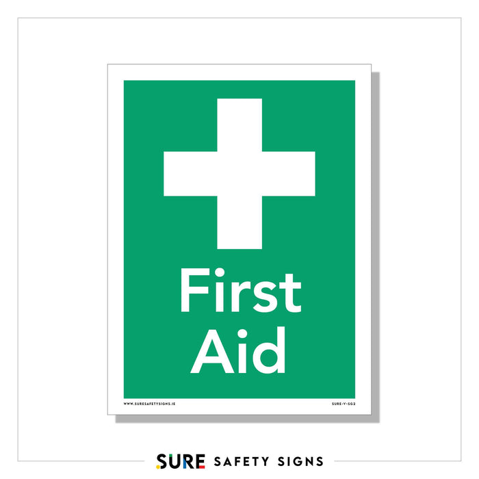 A green sign with a white cross above the bold words First Aid indicates a medical assistance point. The green background signals compliance with safety regulations for identifying aid locations.