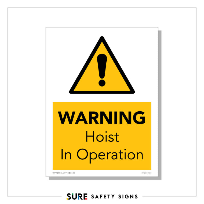 A safety sign featuring a black exclamation mark inside a yellow triangle hovers above the text WARNING Hoist In Operation, boldly displayed in black letters on a yellow background. Found across numerous sites in Ireland, it alerts all to exercise caution as operations proceed.