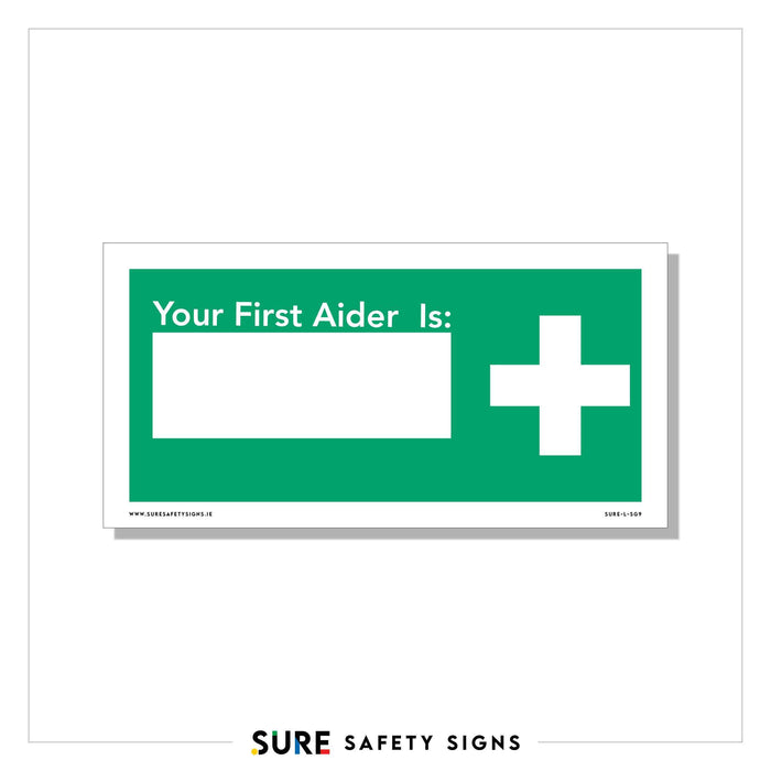 A green and white safety sign from Sure Safety Signs reads Your First Aider Is: with a blank space for a name, alongside a white medical cross. This customizable signage ensures your workplace always knows who the first aider is.